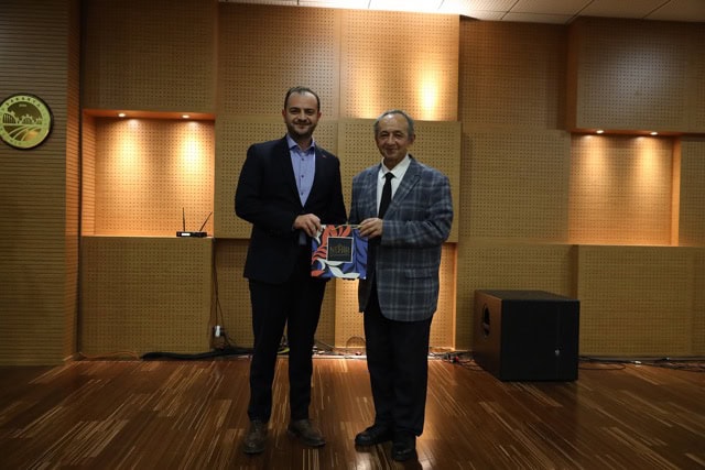 Başın Merkezi logo ve iki kişi el sıkışıyor, ödül veya sertifika takdim ediyor.